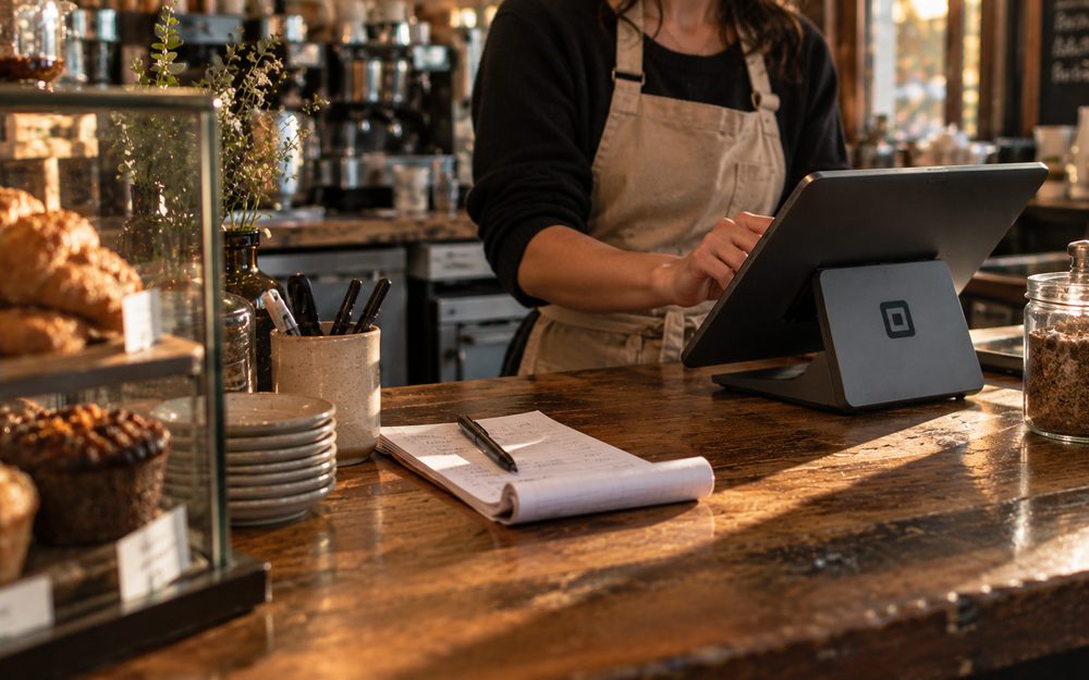 A handwritten receipt pad beside a tablet card reader on a wooden shop counter
